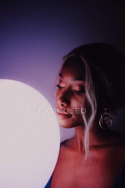 Черная взрослая женщина с белым освещенным воздушным шаром в темноте, глядя в камеру — стоковое фото