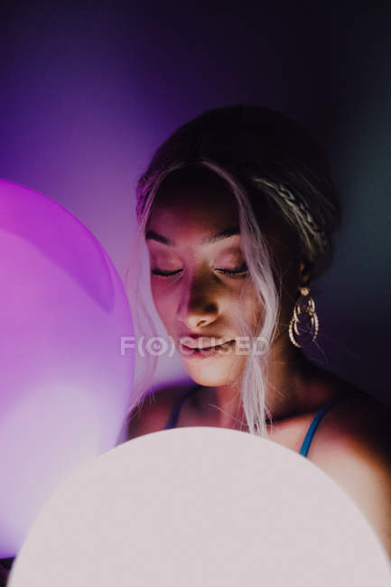 Attractive Black adult woman with white illuminated balloon in darkness looking at camera. - foto de stock