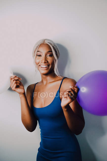 Весела чорна доросла жінка з різнокольоровими кульками дивиться на камеру, стоячи на білому тлі — стокове фото