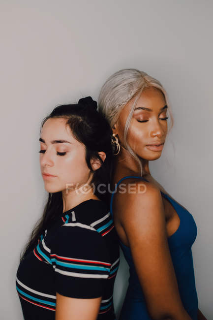 Привабливі молоді жінки з закритими очима стоять один з одним на сірому фоні — стокове фото