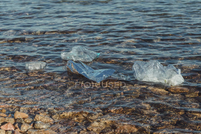 Пустые пластиковые скомканные бутылки отходы, лежащие в чистой воде на берегу моря рядом со скалами — стоковое фото
