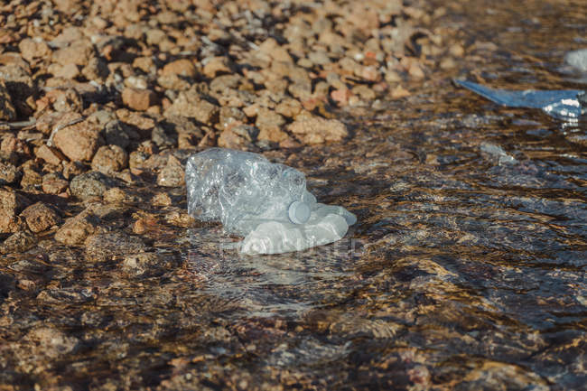 Порожні пластикові збиті пляшки відходи, що лежать у чистій воді на узбережжі біля скель — стокове фото