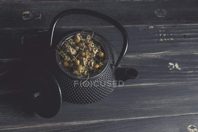 Pilha de margarida seca para fazer chá em bule de metal na mesa escura — Fotografia de Stock