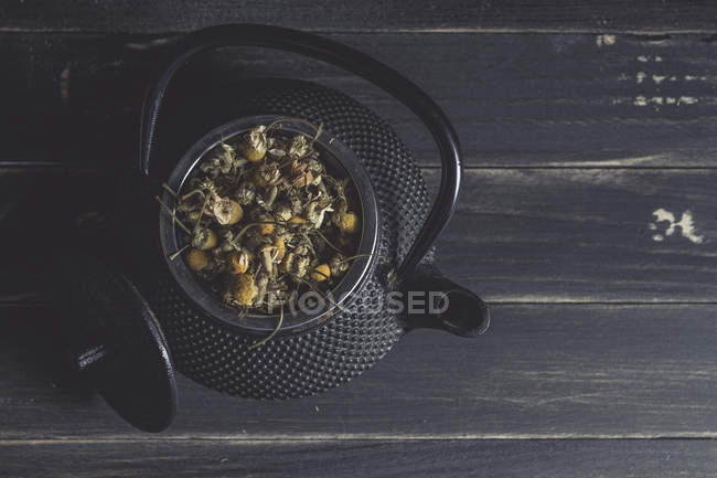 Сушеная ромашка для приготовления чая в металлическом чайнике на темном столе — стоковое фото