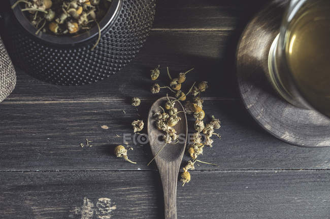 Зверху сухої ромашки в ложці на темному дерев'яному столі біля чашки з трав'яним чаєм — стокове фото