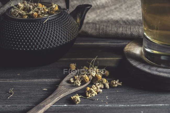 Сверху сушеная маргаритка в ложке на темном деревянном столе возле чашки с травяным чаем — стоковое фото