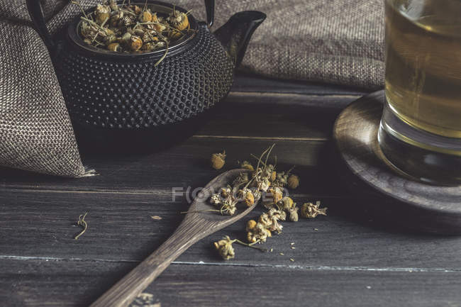 De dessus de marguerite séchée dans cuillère sur table en bois sombre près de tasse avec tisane — Photo de stock