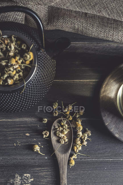 Von oben getrocknetes Gänseblümchen in Löffel auf dunklem Holztisch neben Tasse mit Kräutertee — Stockfoto