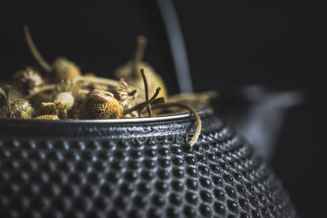 Gros plan de tas de marguerites séchées pour la fabrication du thé dans une théière en métal sur une table noire — Photo de stock