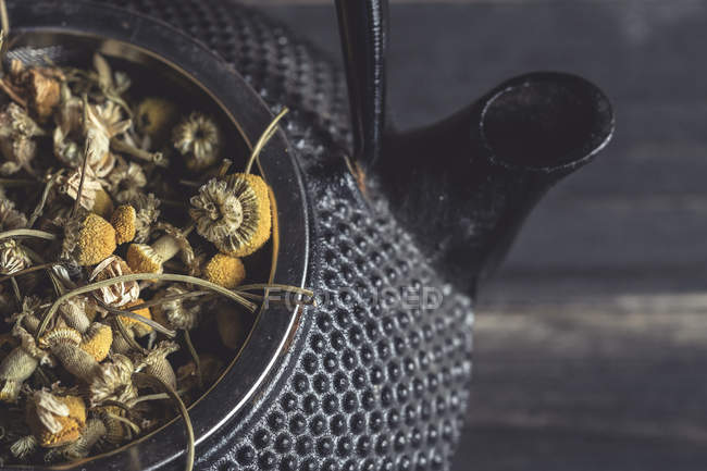Gros plan de tas de marguerites séchées pour la fabrication du thé dans une théière en métal sur une table noire — Photo de stock