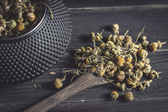 Крупный план сушеной ромашки в деревянной ложке на темном столе для приготовления чая — стоковое фото