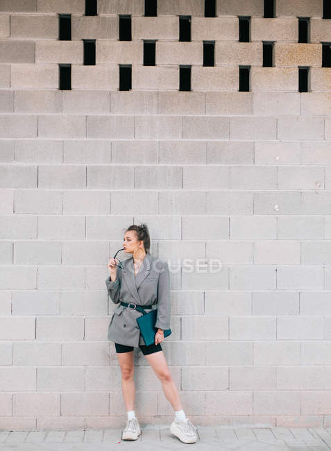 Businesswoman with trendy hairstyle, sunglasses and suit holding laptop and looking away on wall — Stock Photo
