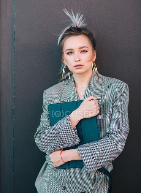Businesswoman with trendy hairstyle and suit holding laptop and looking at camera on wall — Stock Photo