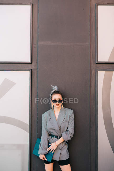 Geschäftsfrau mit trendiger Frisur, Sonnenbrille und Anzug, Laptop in der Hand und Kamera an der Wand — Stockfoto