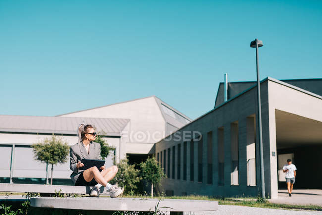 Trendy businesswoman working outside sitting on round decorative panel plates nearby building in bright day — Stock Photo