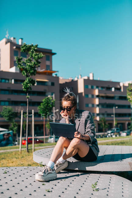 Trendy Geschäftsfrau arbeitet draußen, sitzt auf runden dekorativen Platten in der Nähe Gebäude bei hellem Tag — Stockfoto