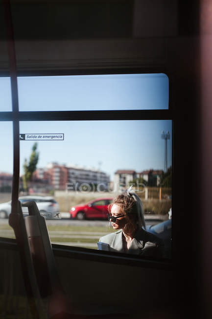 Trendy businesswoman with tablet and sunglasses leaning behind bus and looking away — Stock Photo