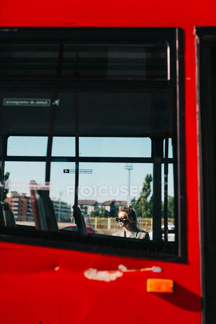 Femme d'affaires branchée en lunettes de soleil penchée derrière le bus et regardant ailleurs — Photo de stock