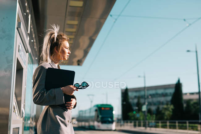 Side view of stylish trendy businesswoman waiting for train and tensely looking away at station — Stock Photo