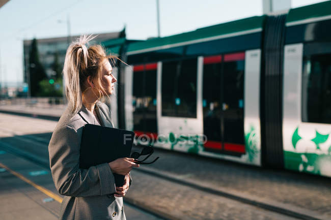 Seitenansicht einer stilvollen trendigen Geschäftsfrau, die auf den Zug wartet und gespannt auf den Bahnhof blickt — Stockfoto