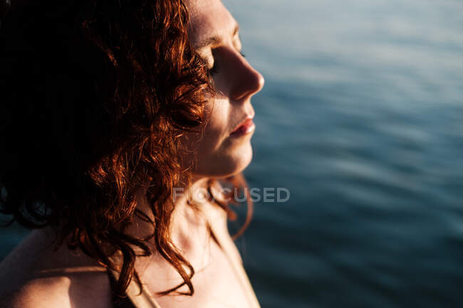 Вид збоку красивої леді з закритими очима, що стоять у чистій морській воді в сонячний день — стокове фото