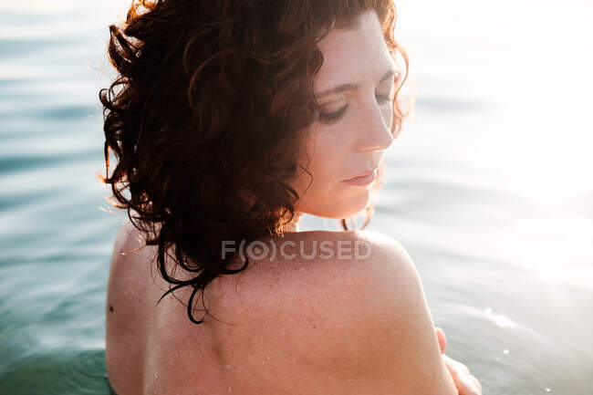 Vue latérale de belle dame regardant au-dessus de l'épaule tout en se tenant dans de l'eau de mer propre le jour ensoleillé — Photo de stock