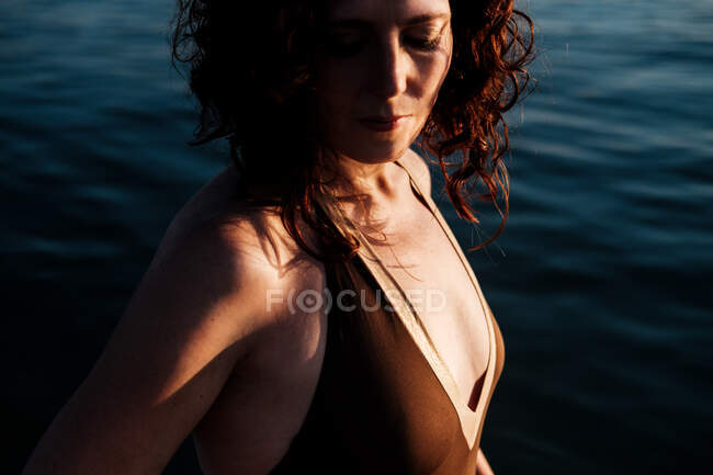 Vista lateral de la hermosa dama con los ojos cerrados de pie en agua de mar limpia en el día soleado - foto de stock