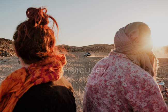 Back view of unrecognizable tourists looking at distant car while spending time in arid desert in Morocco — Foto stock
