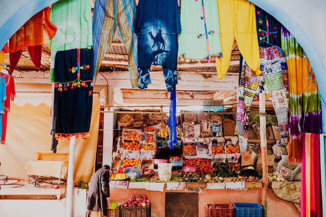 Анонімний чоловік стоїть біля стайні з різними свіжими фруктами та овочами в сонячний день на традиційному базарі в Марокко. — стокове фото