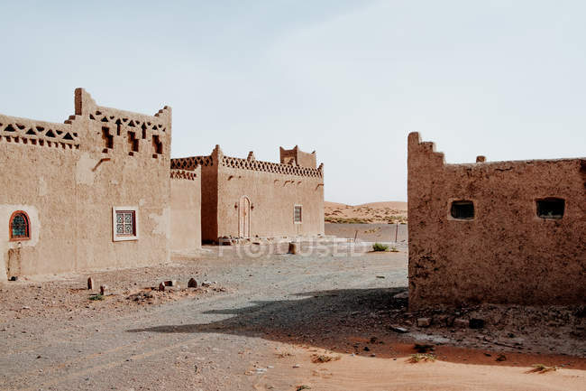 Exterior de edifícios árabes tradicionais shabby com ornamentos localizados na rua de pequena cidade contra céu sem nuvens em Marrocos — Fotografia de Stock