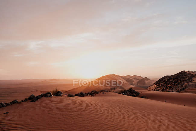 Cloudy sundown sky over hills and rocks in arid desert in evening in Morocco. - foto de stock