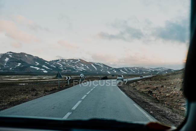 Estrada asfáltica passando por planícies e colinas em frente ao veículo no dia cinzento nublado em Marrocos — Fotografia de Stock