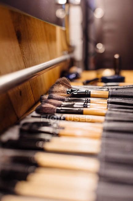 Focus morbido di diversi pennelli e strumenti per il trucco professionale disposti su tavolo in legno su sfondo sfocato — Foto stock