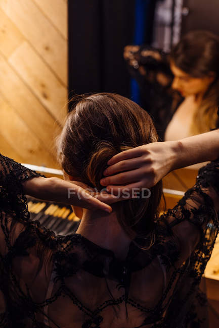 Vista posteriore della donna bruna che fissa i capelli mentre lo stilista del raccolto sta dietro e riflette nello specchio nello spogliatoio — Foto stock