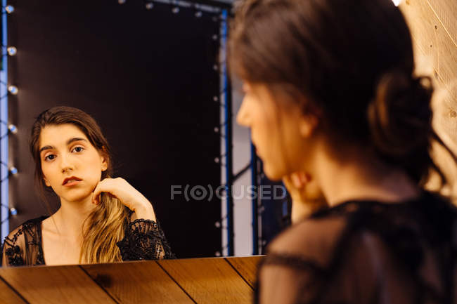 Вид ззаду сумна приваблива жінка в мереживному пігирі сидить у роздягальні, дивлячись у дзеркало і роблячи волосся — стокове фото
