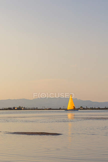 Bright yacht going under yellow sail in calm water at sunrise on nature background — Stock Photo