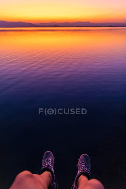 Ноги неузнаваемого туриста висят над спокойной морской водой во время яркого заката — стоковое фото