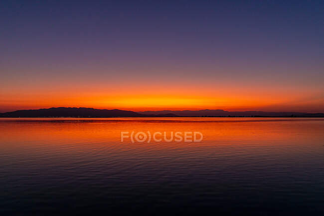Cielo sin nubes brillante puesta de sol sobre la costa distante y la superficie tranquila del lago en la naturaleza - foto de stock