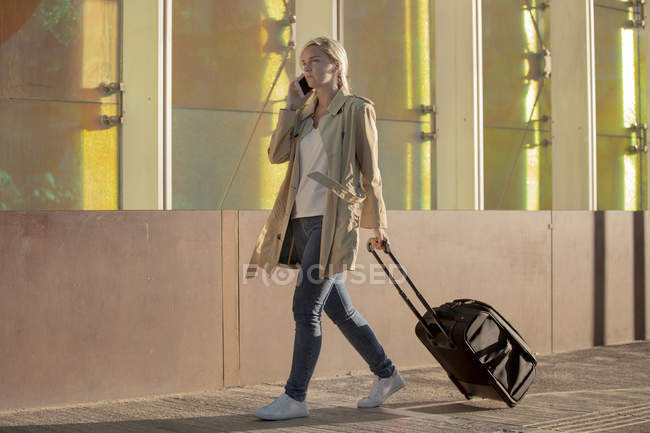 Vista laterale della giovane turista in impermeabile parlando su smartphone mentre si cammina in strada — Foto stock