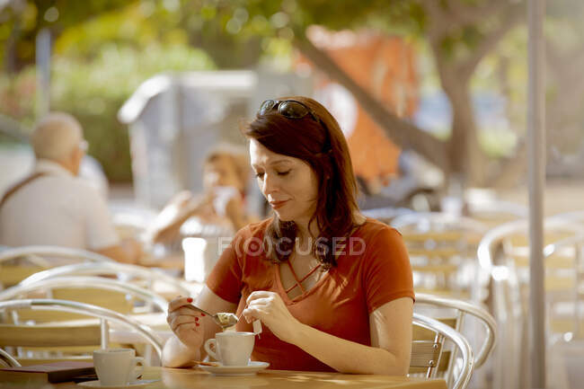 Свободная женщина, заваривающая чай, сидя на уютной летней террасе кафе и обедая — стоковое фото