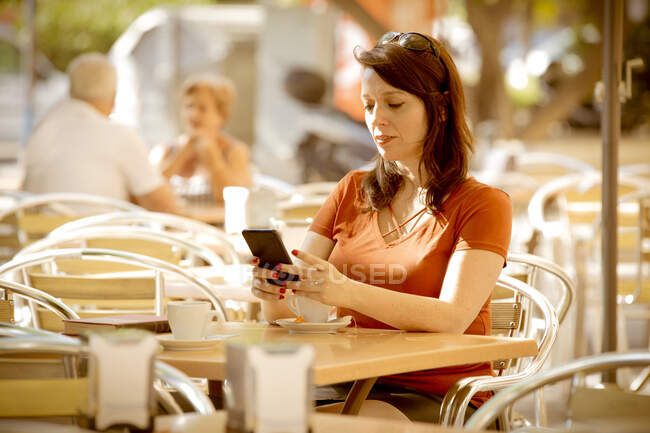 Дорослі спокійні жінки у повсякденному одязі серфінг Інтернету, сидячи на затишній літній терасі кафе і чекаючи на порядок. — стокове фото