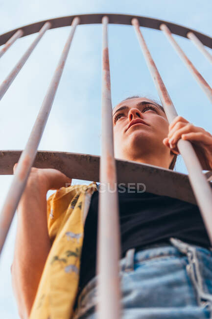 From below sensual casual woman standing in cage on clear sky in summer and looking away — Stock Photo