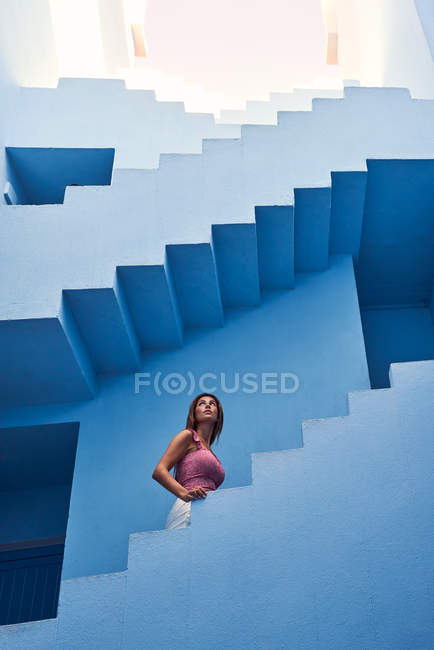 Vista lateral de la mujer caminando arriba en el moderno edificio azul y mirando hacia arriba - foto de stock