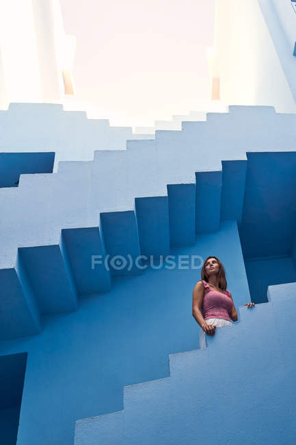 Vista lateral de la mujer caminando arriba en el moderno edificio azul y mirando hacia otro lado - foto de stock