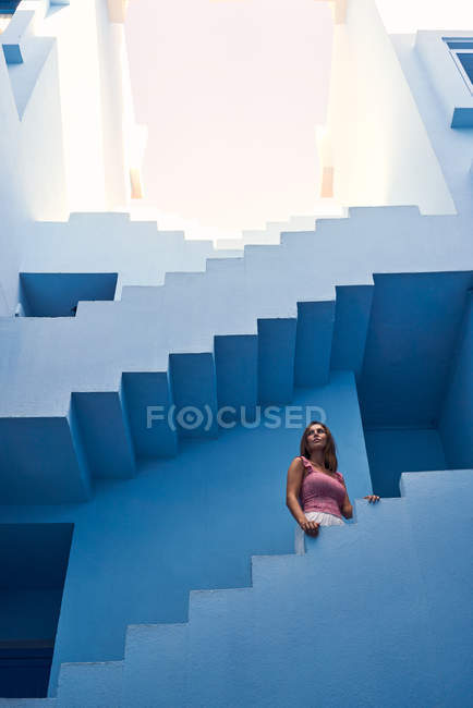 Seitenansicht einer Frau, die auf einem modernen blauen Gebäude nach oben geht und wegschaut — Stockfoto
