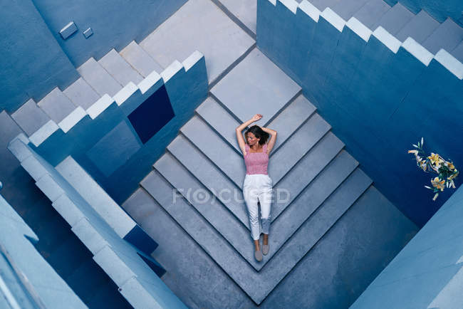 Вид сверху на женщину, лежащую на синей лестнице и отводящую взгляд — стоковое фото