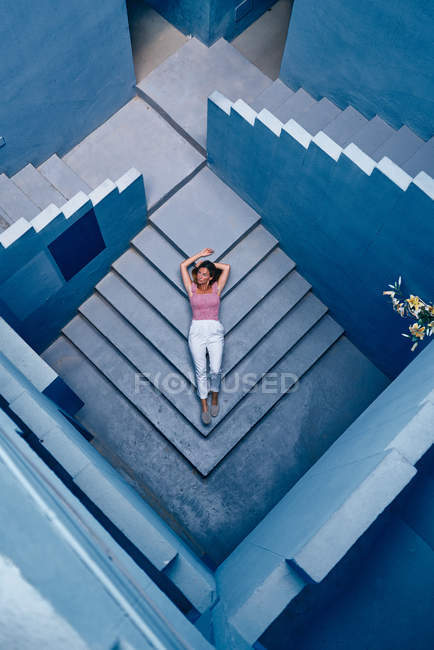 Вид зверху на жінку, що лежить на блакитних сходах і дивиться в сторону — стокове фото