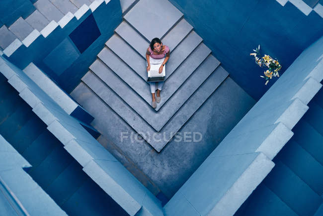 Top view of Beautiful woman sitting on blue staircase of blue building and using computer — Stock Photo