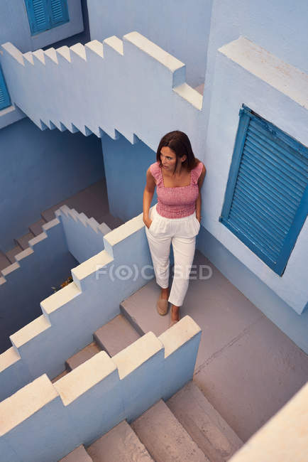 Vista superior de la joven mujer caminando arriba en el moderno edificio azul y mirando hacia otro lado - foto de stock