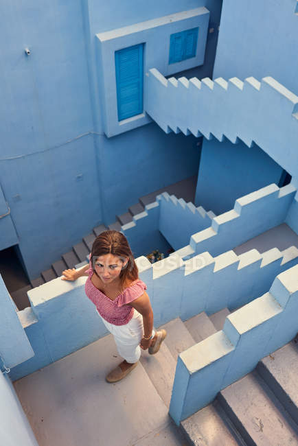 De cima vista da jovem mulher andando no andar de cima no moderno edifício azul e olhando para longe — Fotografia de Stock